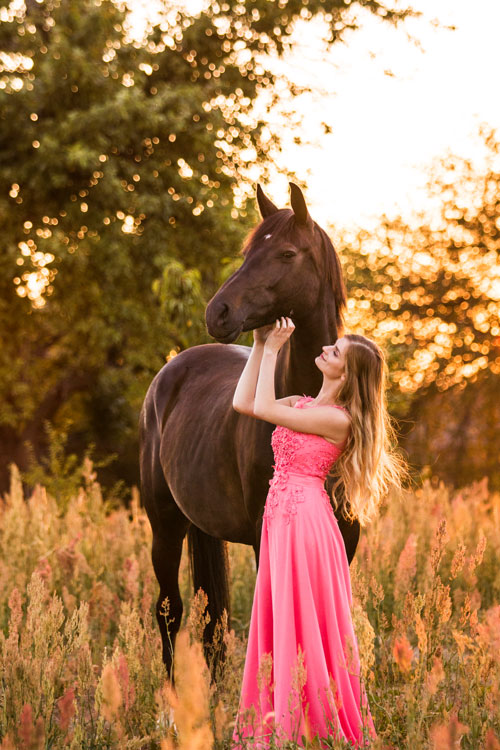 Mädchen im Kleid mit Pferd im Sonnenuntergang